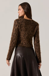 A woman is wearing a long-sleeved, fuzzy brown sweater with a subtle leopard print pattern, paired with a high-waisted, dark leather A-line skirt.